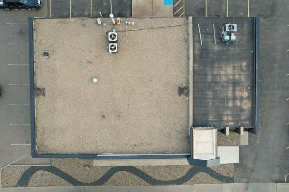 Aerial view of a commercial building with an old weathered flat roof before Quest Exteriors work